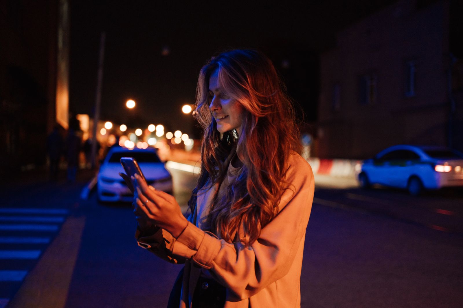 A woman smiling at her phone with city lights behind her