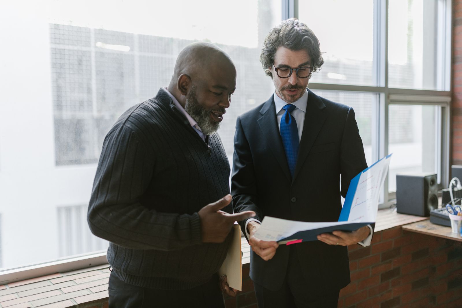 Two colleagues reviewing documents by an office window
